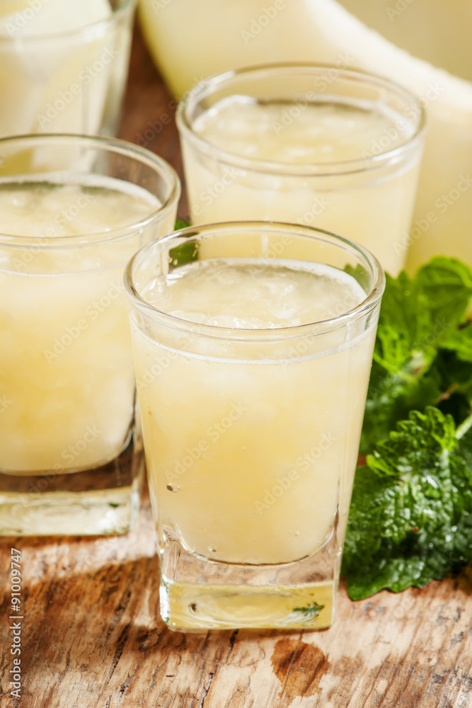 Melon juice in a glass, mint and slices of melon on a wooden ba Melon juice in a glass, mint and slices of melon on a wooden ba