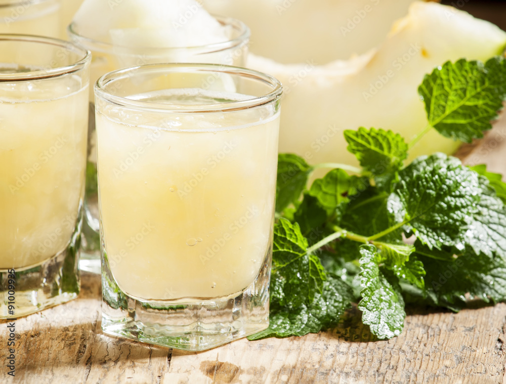 Melon juice in a glass, mint and slices of melon on a wooden ba Melon juice in a glass, mint and slices of melon on a wooden ba