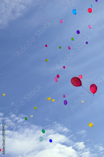 Many colored balloons fly in the blue sky with clouds