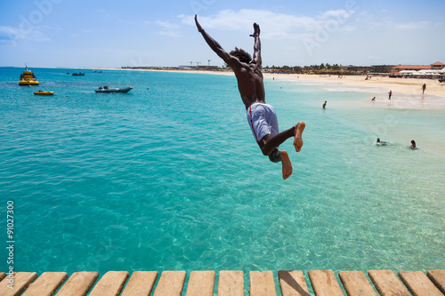 Teenage Cape verdean boy jumping on the turquoise  water of Sant photo