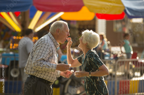 Happy fun woman feeding husband snack at amusement park fun fair