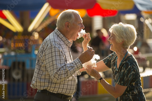 Happy fun woman feeding husband cotton candy snack at amusement park fun fair