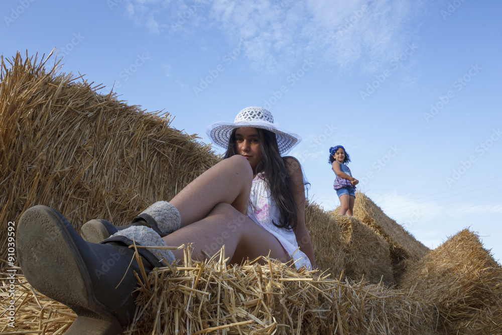 Niña pequeña y adolescente en las alpacas de heno al final de verano. Dos hermanas disfrutando en el campo de una tarde de verano. Niña pequeña y adolescente en las alpacas de heno al final de verano. Dos hermanas disfrutando en el campo de una tarde de verano.