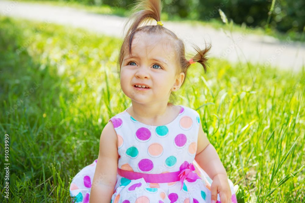 Cute little girl wearing polka dots dress sitting on the grass Cute little girl wearing polka dots dress sitting on the grass