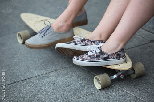 Feet couple of teenagers in sneakers on longboard closeup