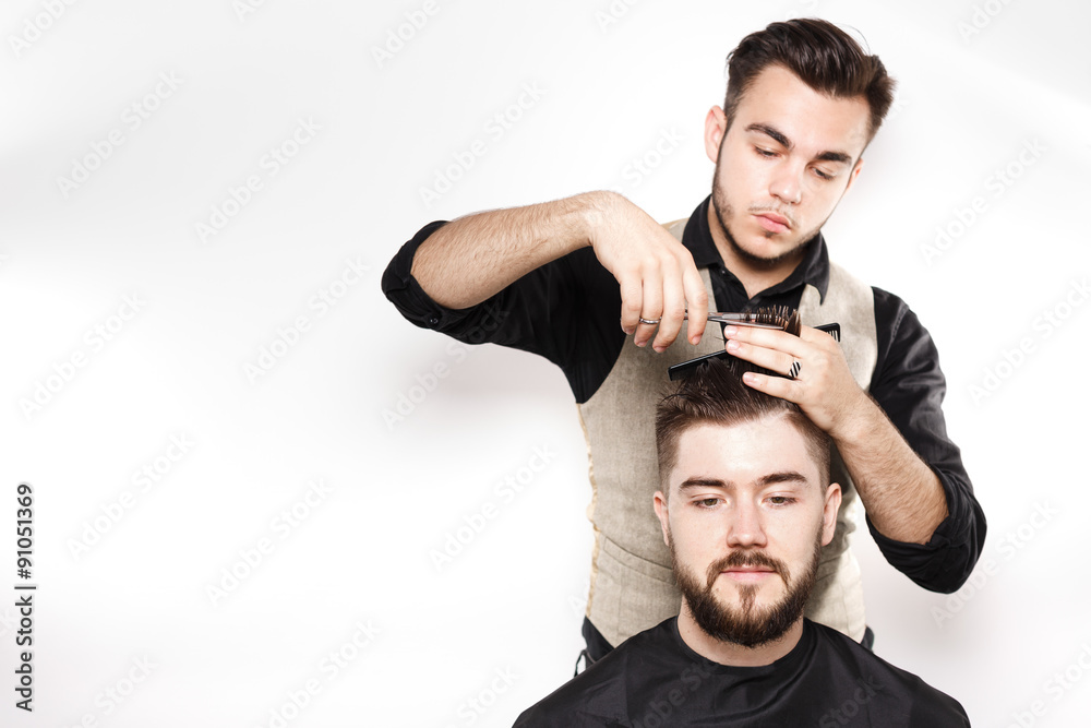 Young barber cuts hair on head of brunette bearded client Young barber cuts hair on head of brunette bearded client