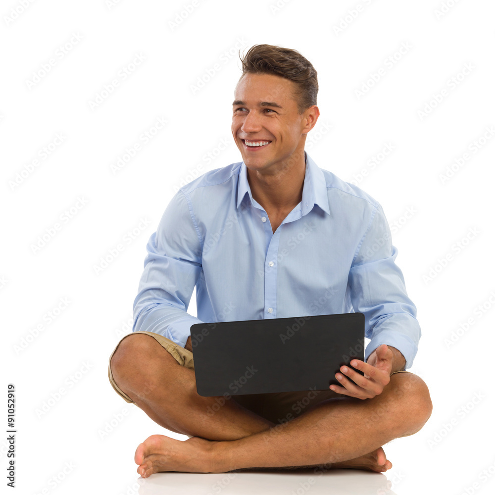 Just Take A Break. Smiling young man in blue shirt holds laptop on his crossed legs and looking away. Full length studio shot isolated on white. Just Take A Break. Smiling young man in blue shirt holds laptop on his crossed legs and looking away. Full length studio shot isolated on white.