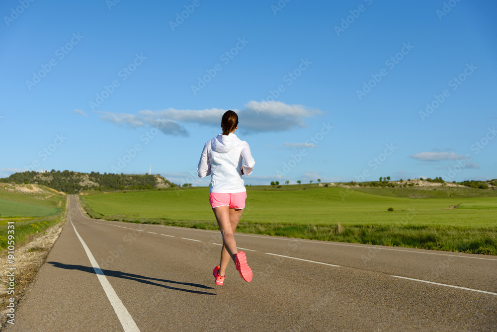 Sporty woman running on country side road back view. Female athlete training outdoor.