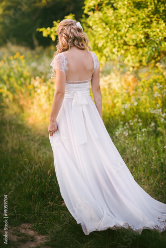 Stylish beautiful blonde bride standing in her wedding dress back to nature in the sunset light, wedding, marriage, tenderness, woman, lifestyle