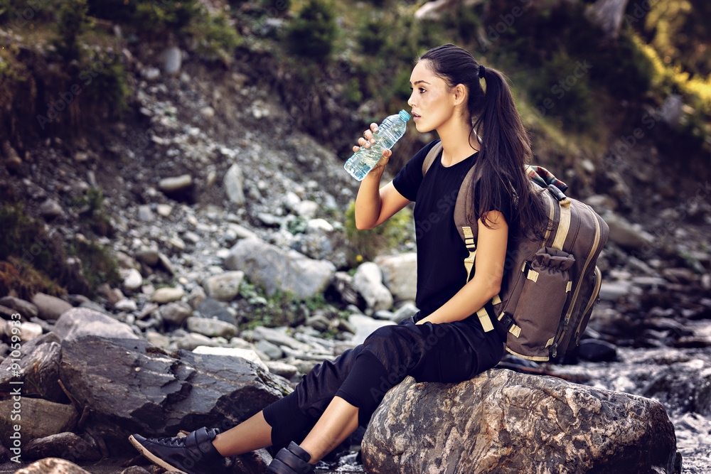 beautiful woman resting on a rock in the river and drinking wate