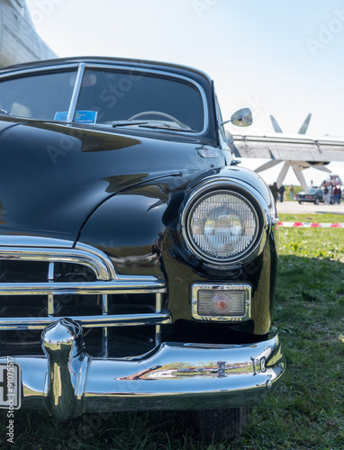 Headlight and bumper of a black retro car. Close-up, front view, outdoor scene.