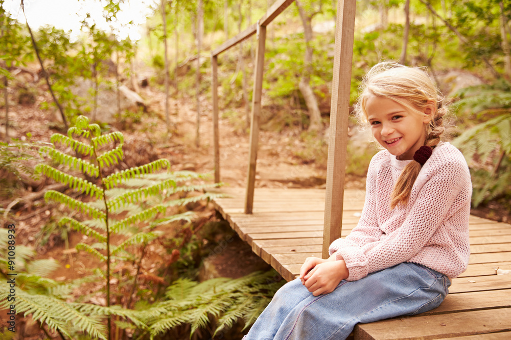 Obraz premium Smiling young girl sitting on a wooden bridge in a forest