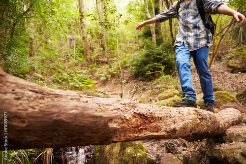 Boy balancing on a fallen tree to cross a stream in a forest