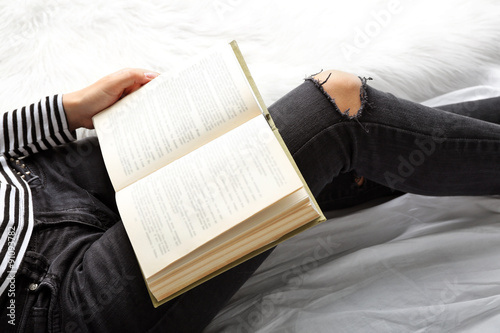 Woman in black jeans reading book on bed top view point