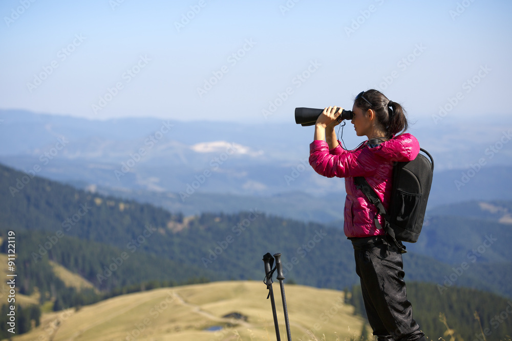 Hiker looking in binoculars enjoying spectacular view on mountai