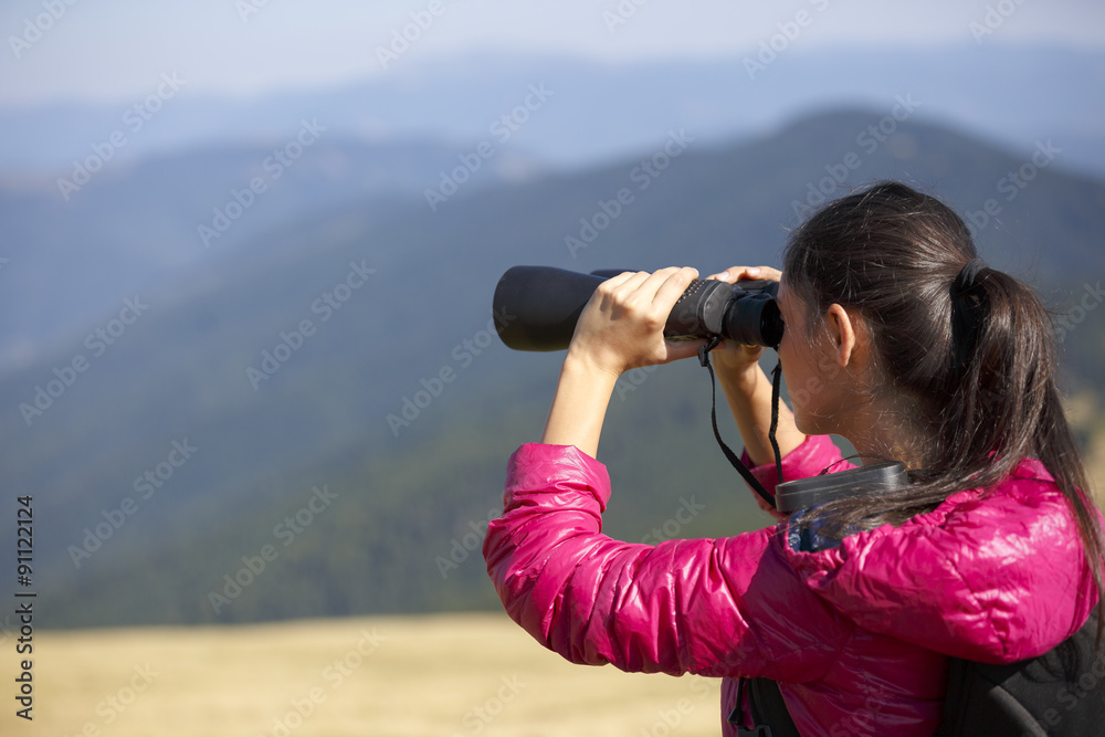 Hiker looking in binoculars enjoying spectacular view on mountai Hiker looking in binoculars enjoying spectacular view on mountai