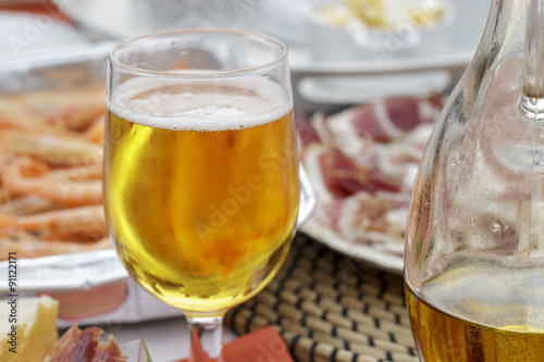 Glass of beer beside a jar of olive oil, shrimps and iberian ham