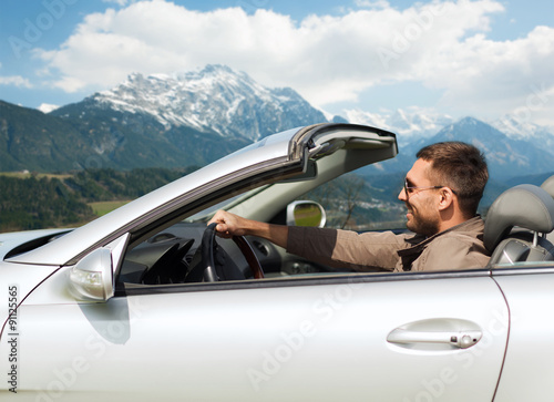 happy man driving cabriolet car over mountains