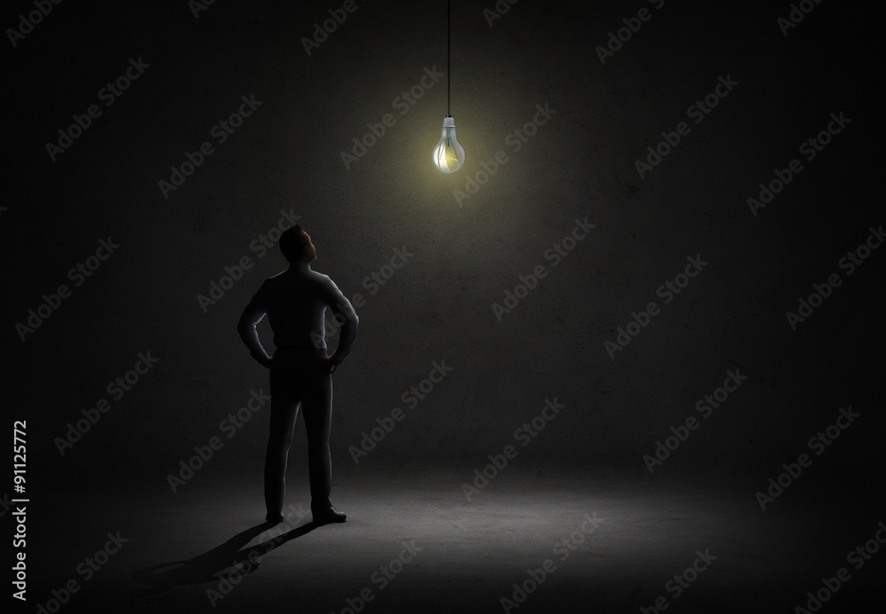 Fototapeta premium businessman looking at lighting bulb in dark room