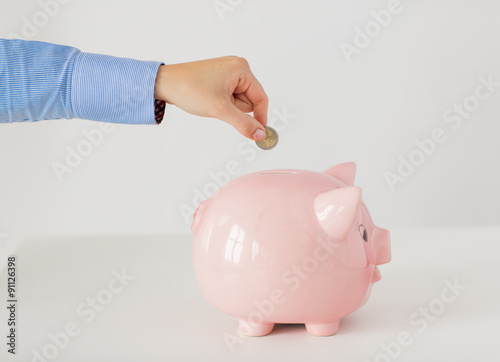 close up of hand putting coin into piggy bank