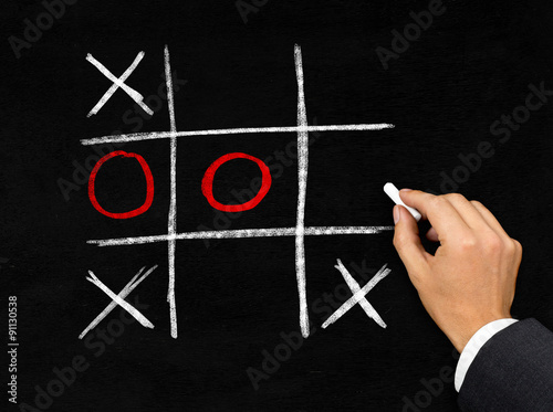 Tic-Tac-Toe game on blackboard by businessman