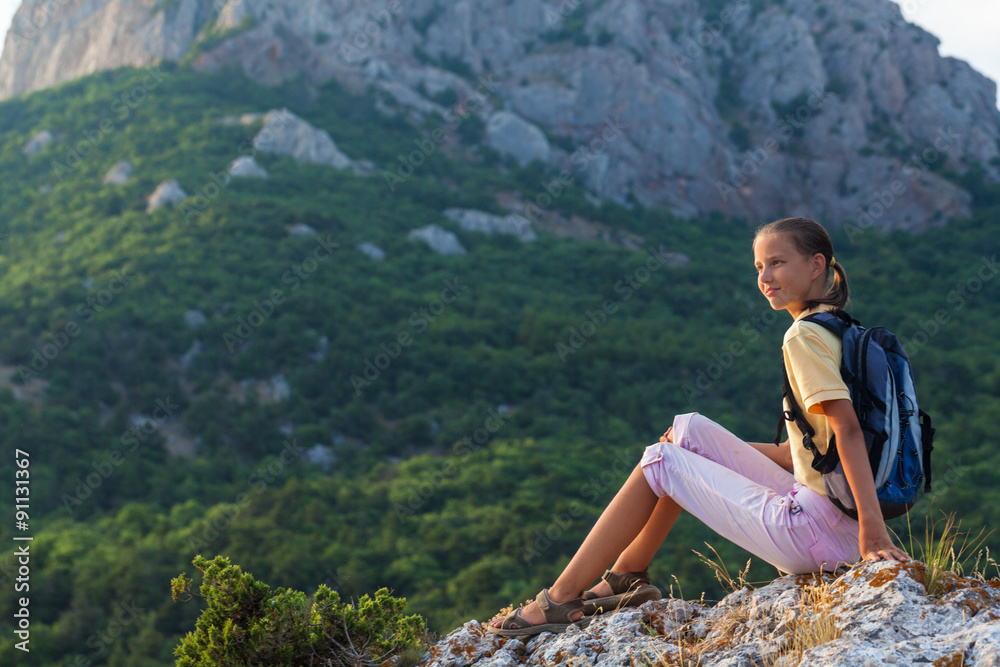 Young woman with backpack sits on a rock