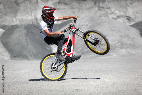 Athlete in a helmet riding a mountain bike on the back wheel in the style of trial
