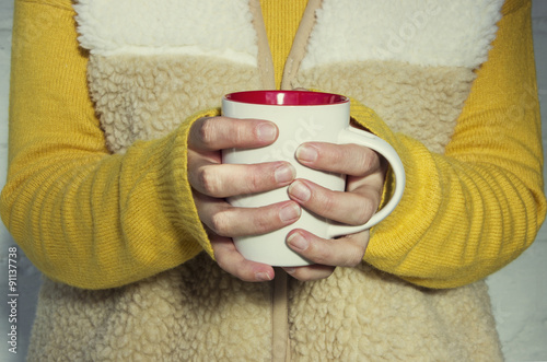 A woman holds a hot cup of tea and warms his hands