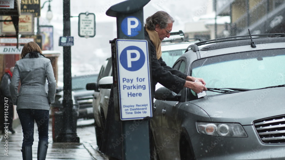 man walking down the street to his car to find a parking ticket on it