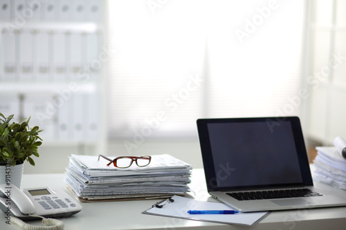 Laptop with stack of folders on table on white background