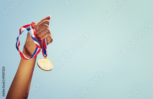 woman hand raised, holding gold medal against sky. award and victory concept photo