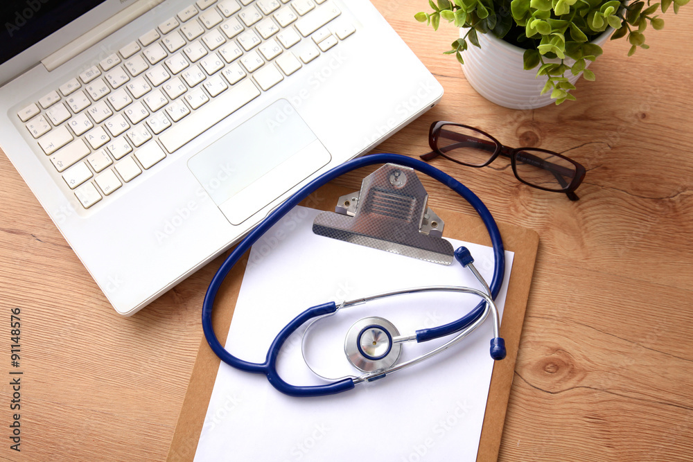 A medical stethoscope near a laptop on a wooden table, on white A medical stethoscope near a laptop on a wooden table, on white