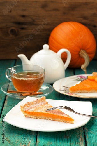 Pumpkin pie, tea in glass cup, white teapot and fresh pumpkin on