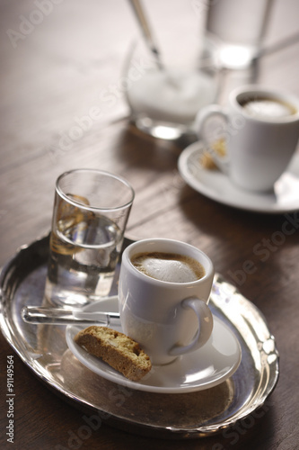 A cup of espresso macchiato with cantuccini and a glass of water