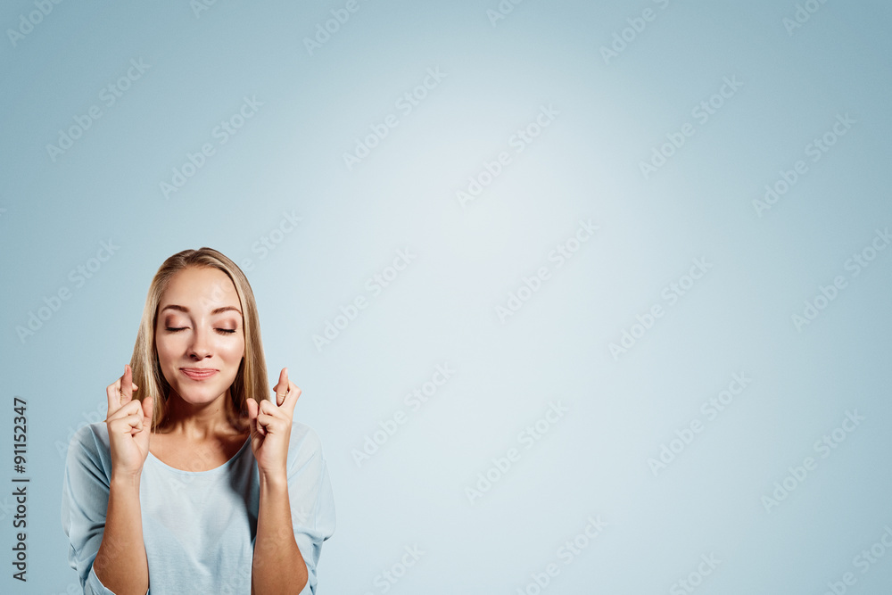 Close-up portrait of a beautiful woman closing her eyes, crossing her fingers hoping for the best,isolated on blue background Close-up portrait of a beautiful woman closing her eyes, crossing her fingers hoping for the best,isolated on blue background