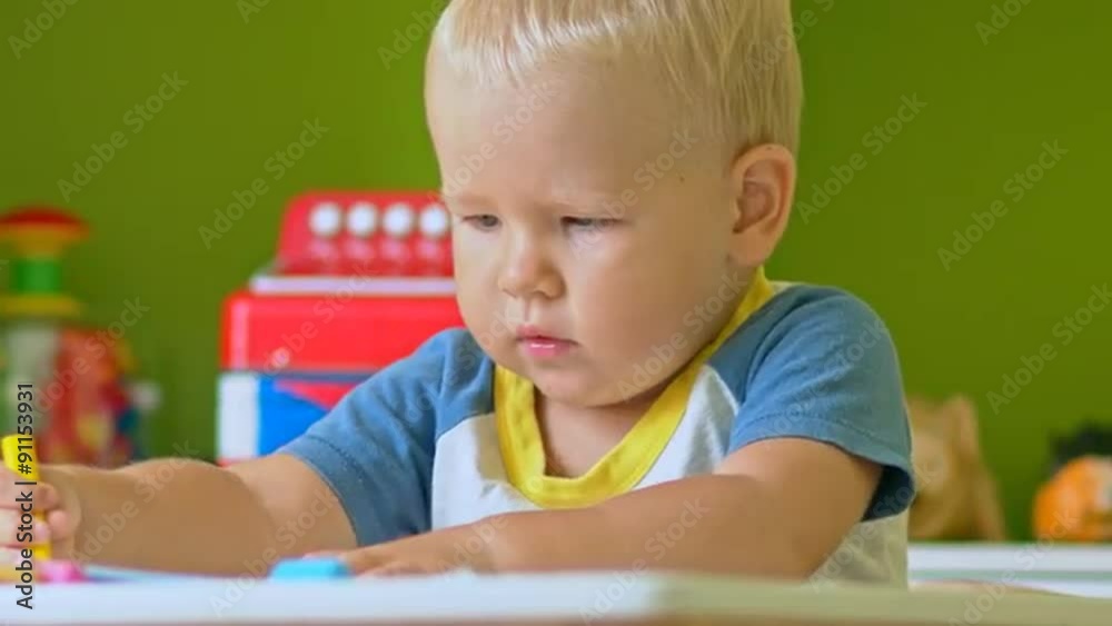 Toddler boy practice to paint with crayons on paper sitting at the table in child room Toddler boy practice to paint with crayons on paper sitting at the table in child room