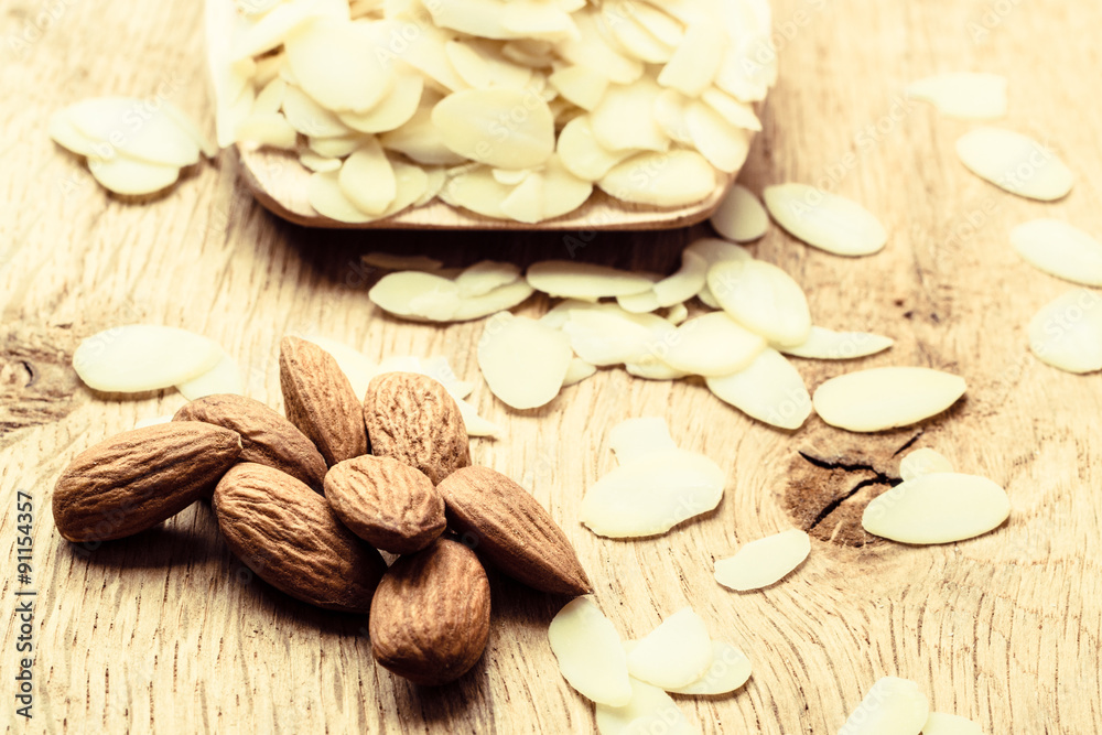 sliced and whole raw almonds on wooden surface