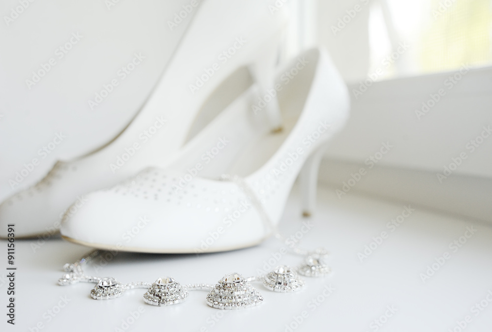White wedding shoes of the bride and the bride's necklace agains White wedding shoes of the bride and the bride's necklace agains