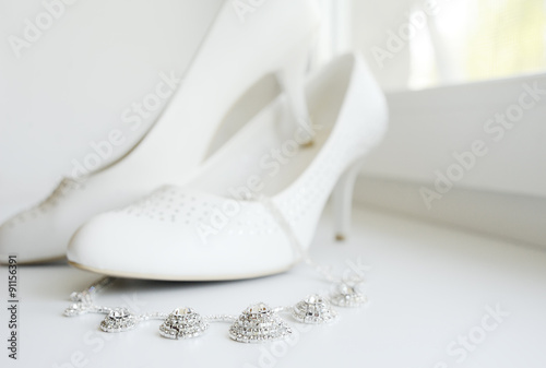 White wedding shoes of the bride and the bride's necklace agains