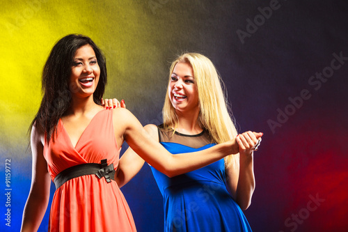 Two funny women holding hands in dresses.