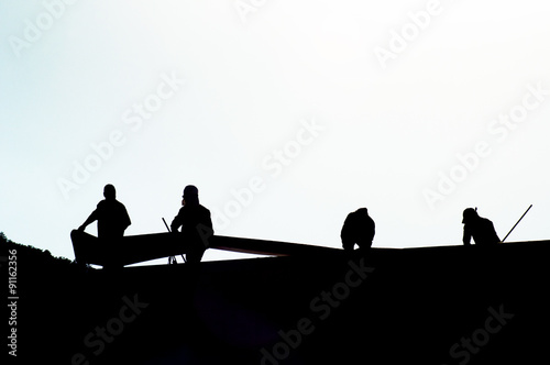 Silhouettes of 4 men roofing a building. © bettys4240