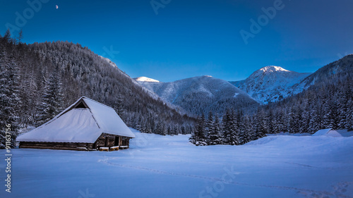 Fototapeta Naklejka Na Ścianę i Meble -  Small mountain cottage in winter valley at sunset