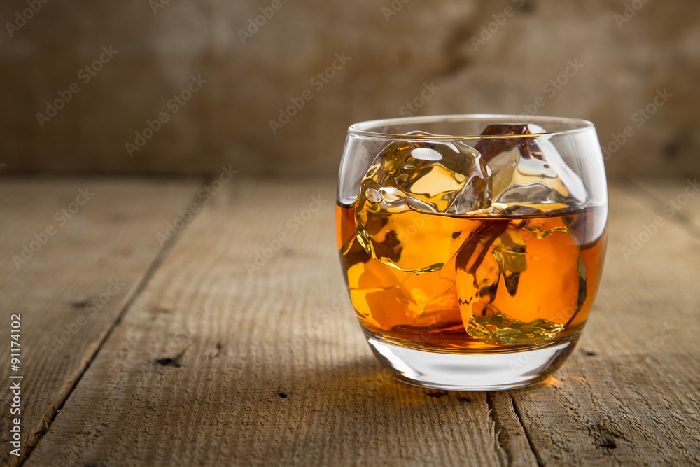 Single glass of whisky bourbon on the rocks golden on old rustic wooden ...