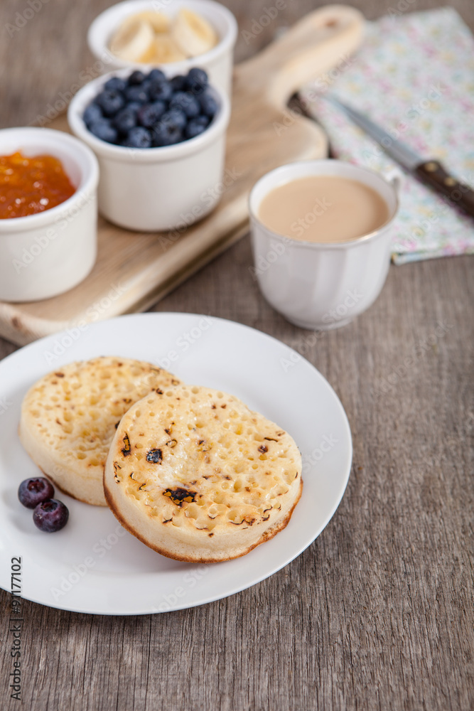 Hot toasted crumpets on the wooden table with blueberries and jam on the back, selective focus Hot toasted crumpets on the wooden table with blueberries and jam on the back, selective focus