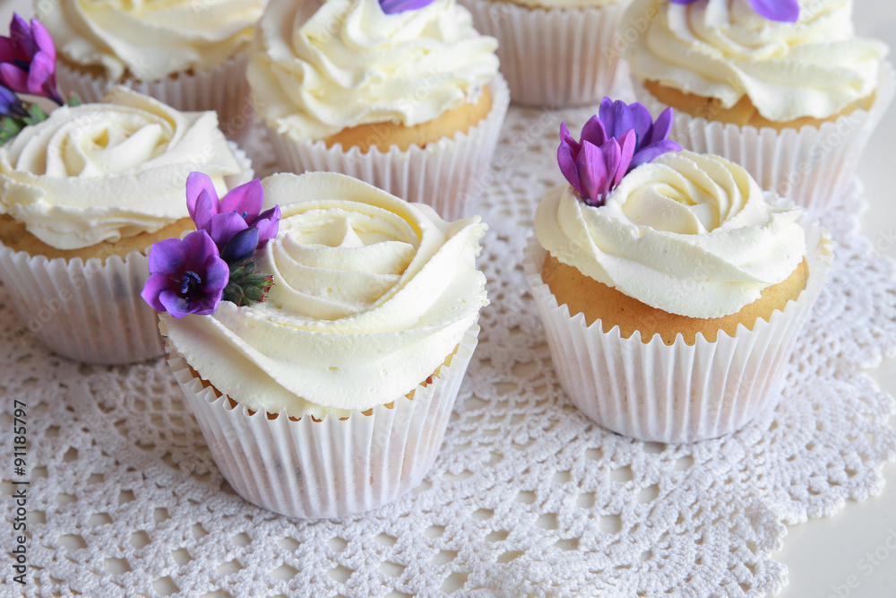 Homemade purple freesia flowers on vanilla cupcakes with whipped