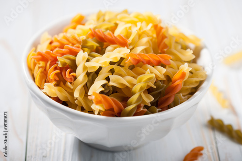 Colorful raw pasta in the bowl on wooden table
