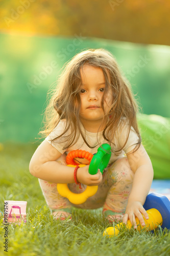 Little girl with toy in hands. Portrait in nature with warm sunl