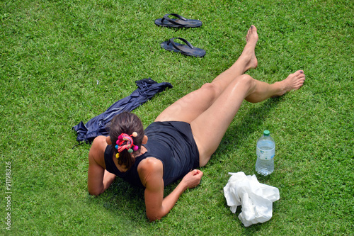 una donna con le gambe denudate prende il sole distesa su un prato
