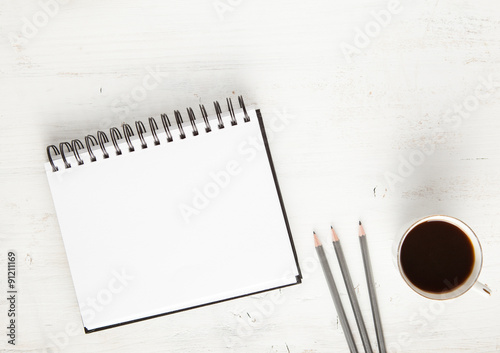 Sketchpad, pencils on the white table, with coffee and chocolate chip cookies on the back, view from above photo