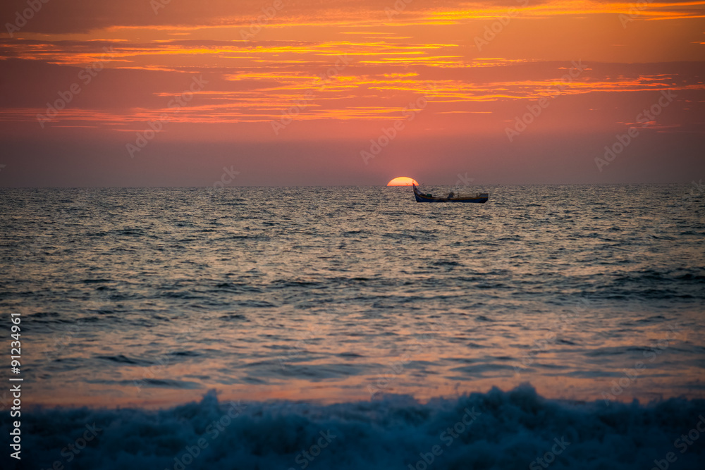 view of sea boat against large sun disk rising from behind sea